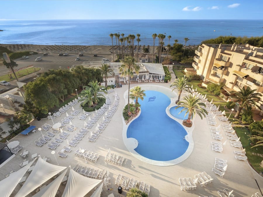 A resort with a large pool, palm trees, and a view of the ocean.