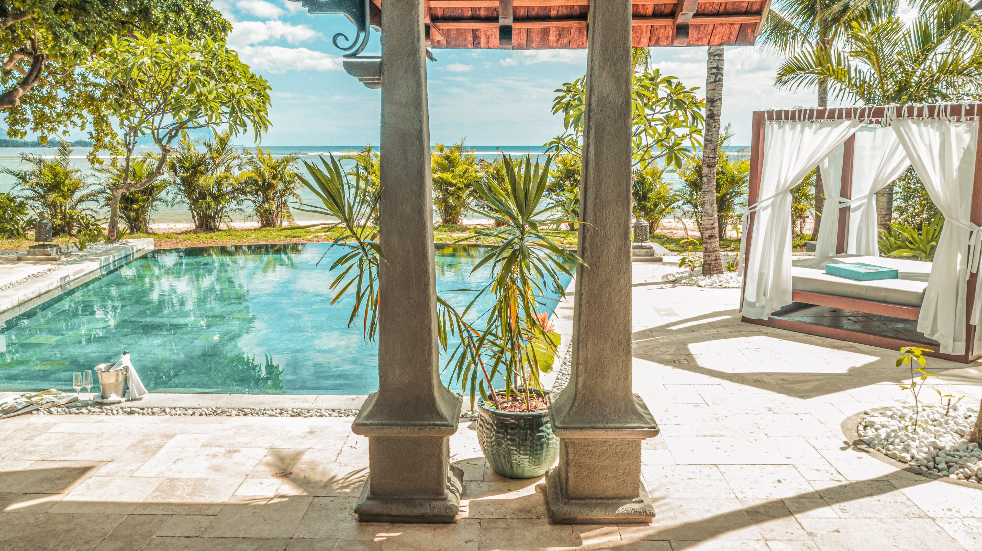 Zona de piscina con vista al océano, rodeada de palmeras y un pabellón.