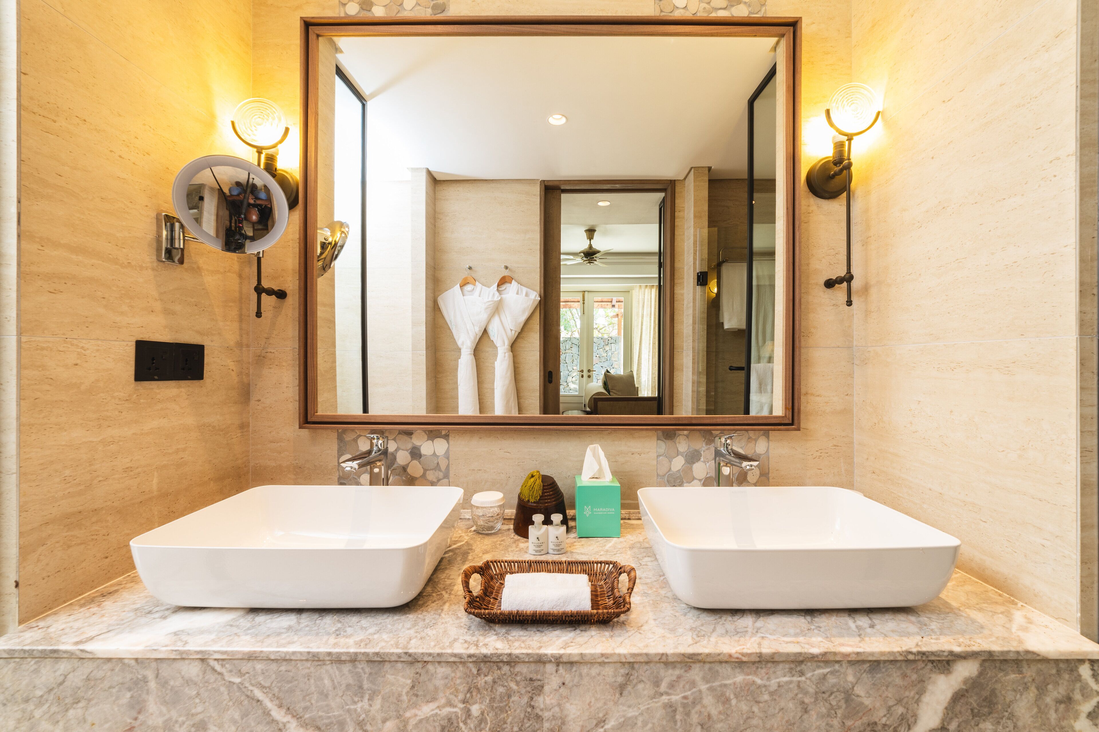 A bathroom with two large white sinks, a mirror, and wall sconces.