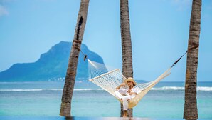 A person relaxing in a hammock between palm trees by the ocean with a mountain in the background. - Maradiva Villas Resort & Spa (Flic-en-Flac)