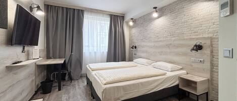 A modern hotel room with a large bed, a desk with a chair, a flat-screen TV, and a brick-patterned wall.