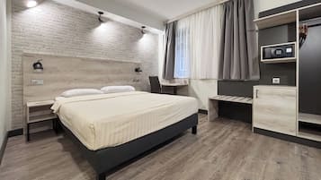 Une chambre d’hôtel moderne, dotée d’un grand lit, d’un bureau, d’une chaise, d’une armoire et d’une petite table.