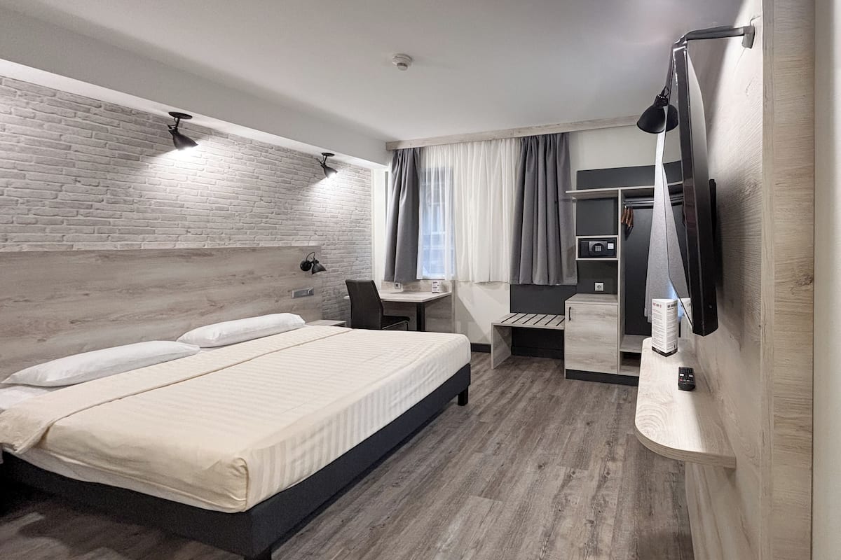 A modern hotel room with a bed, desk, and a TV mounted on the wall.