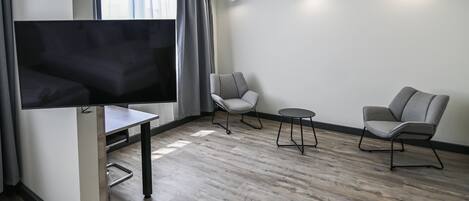 Una sala de estar moderna con un televisor de pantalla plana, dos sillones grises, una mesita redonda y piso de madera.