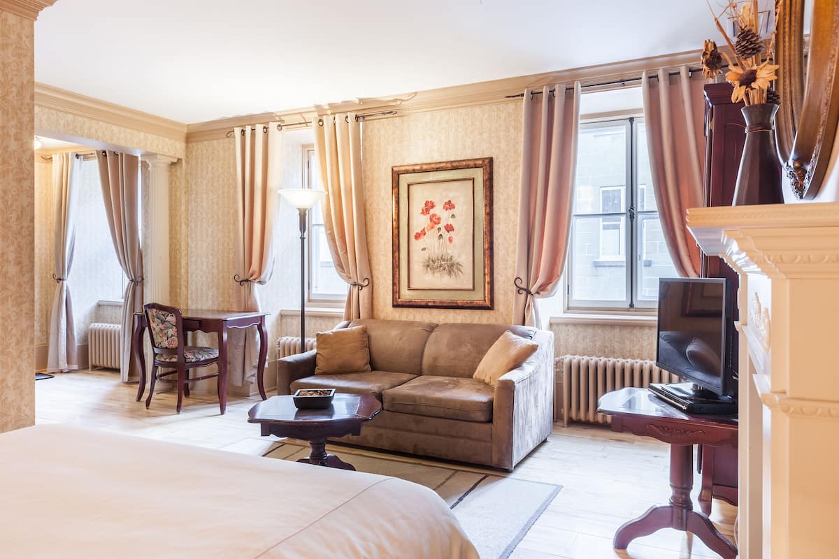 Une chambre d’hôtel avec un grand lit, un canapé, une petite table, une télévision et une fenêtre avec des rideaux.
