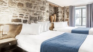 A hotel room with two beds, stone walls, and a large window with curtains. - Hotel Louisbourg (Québec City)
