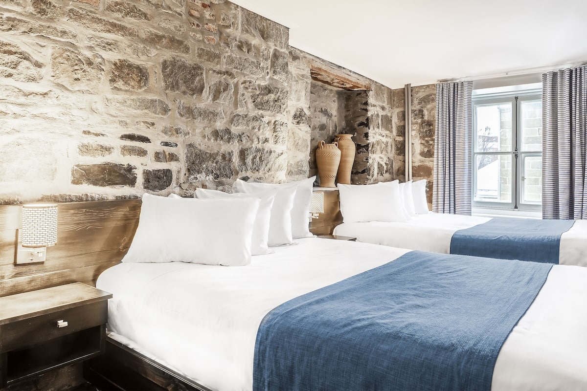Une chambre d’hôtel avec deux lits, des murs en pierre et une grande fenêtre avec des rideaux.