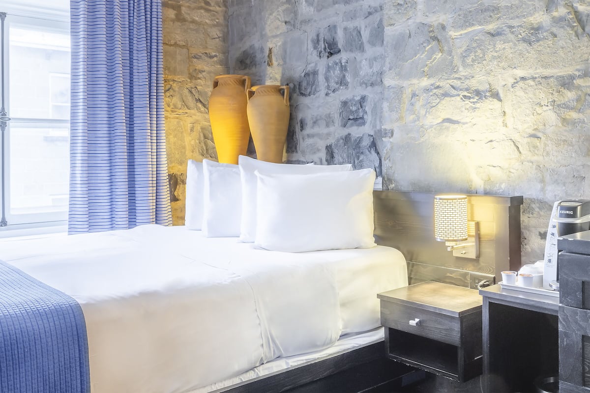 Une chambre d’hôtel avec un grand lit, une table de chevet avec une machine à café et deux grands vases accrochés au mur.