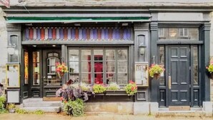 A building with a green awning, a black door, and flower baskets on the windowsills. - Hotel Louisbourg (Québec City)