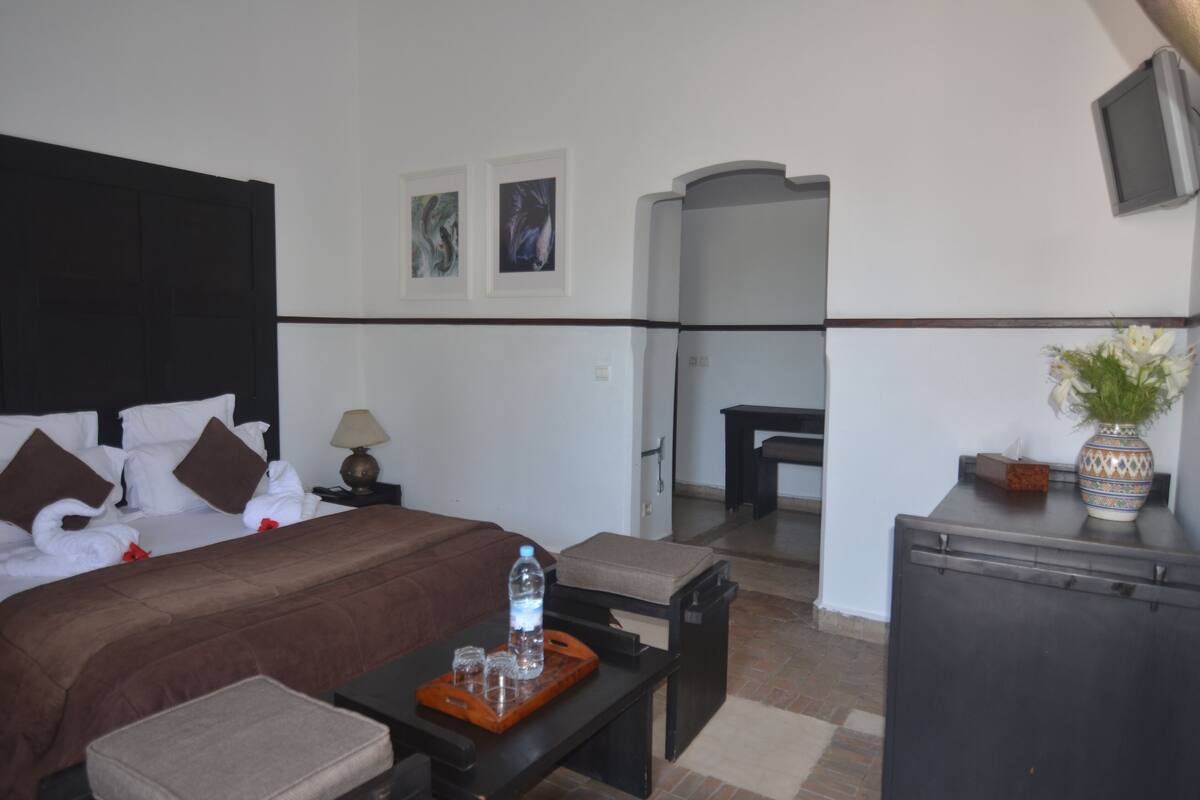 A hotel room with a bed, bedside table, and a small sitting area.