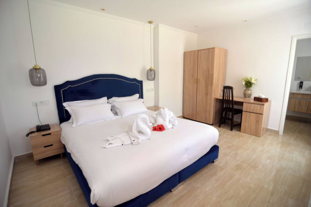A hotel room with a large bed, a desk, and a wardrobe.