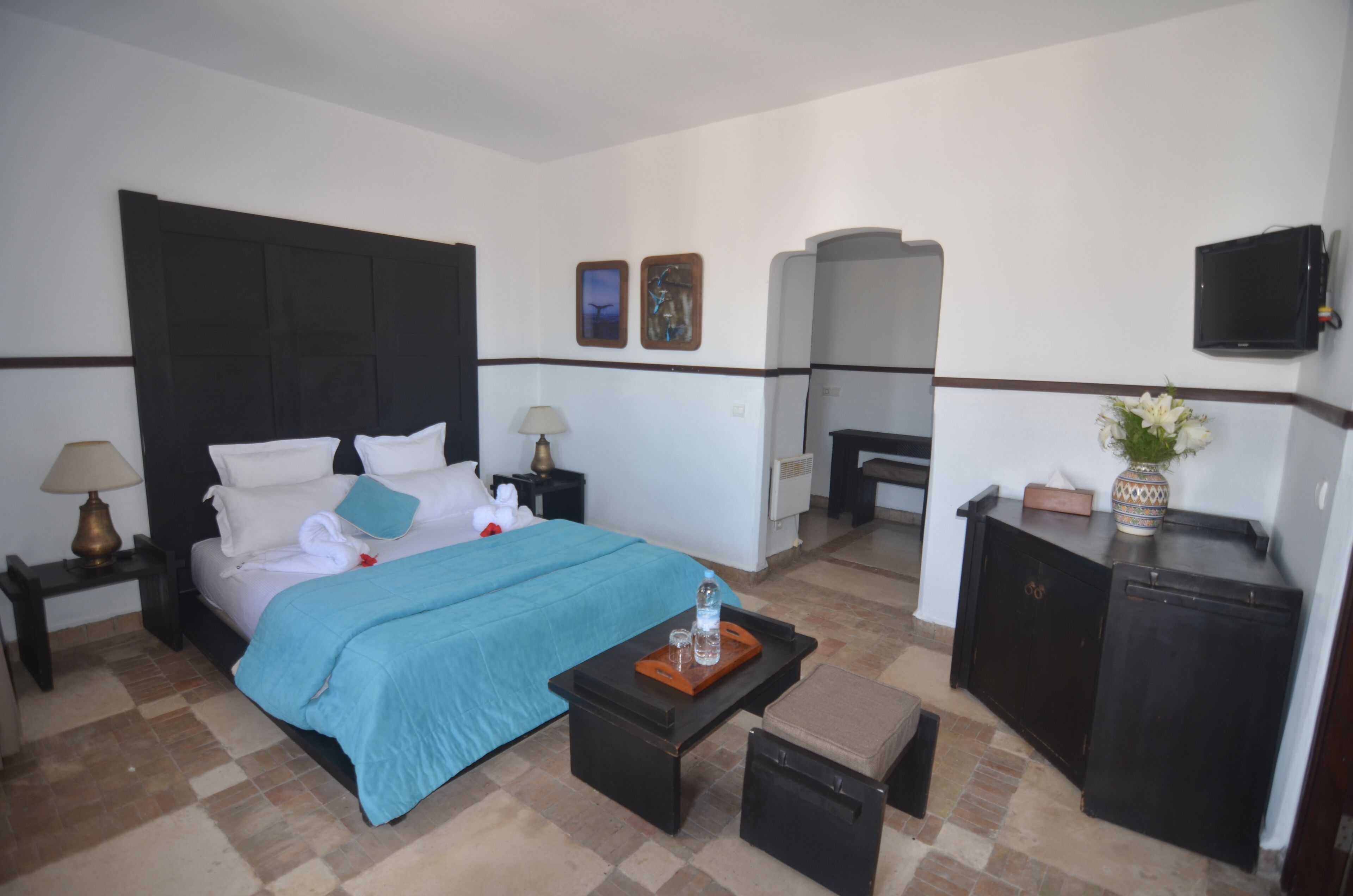 Ein Hotelzimmer mit Bett, Nachttischen, Fernseher, einer kleinen Kommode und einer dekorativen Vase.