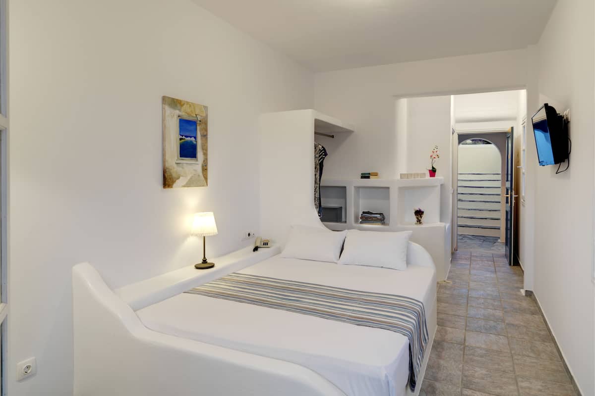 A hotel room with a bed, a lamp, a painting, and a hallway leading to a staircase.