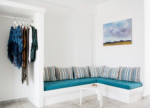 A modern living room with a teal sofa, striped pillows, a white coffee table, and a clothing rack with various garments. - Aloni Hotel (Paros)