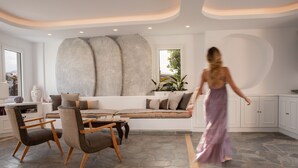 A modern living room with a stone floor, a sofa set, and a large abstract wall art piece. - Aloni Hotel (Paros)