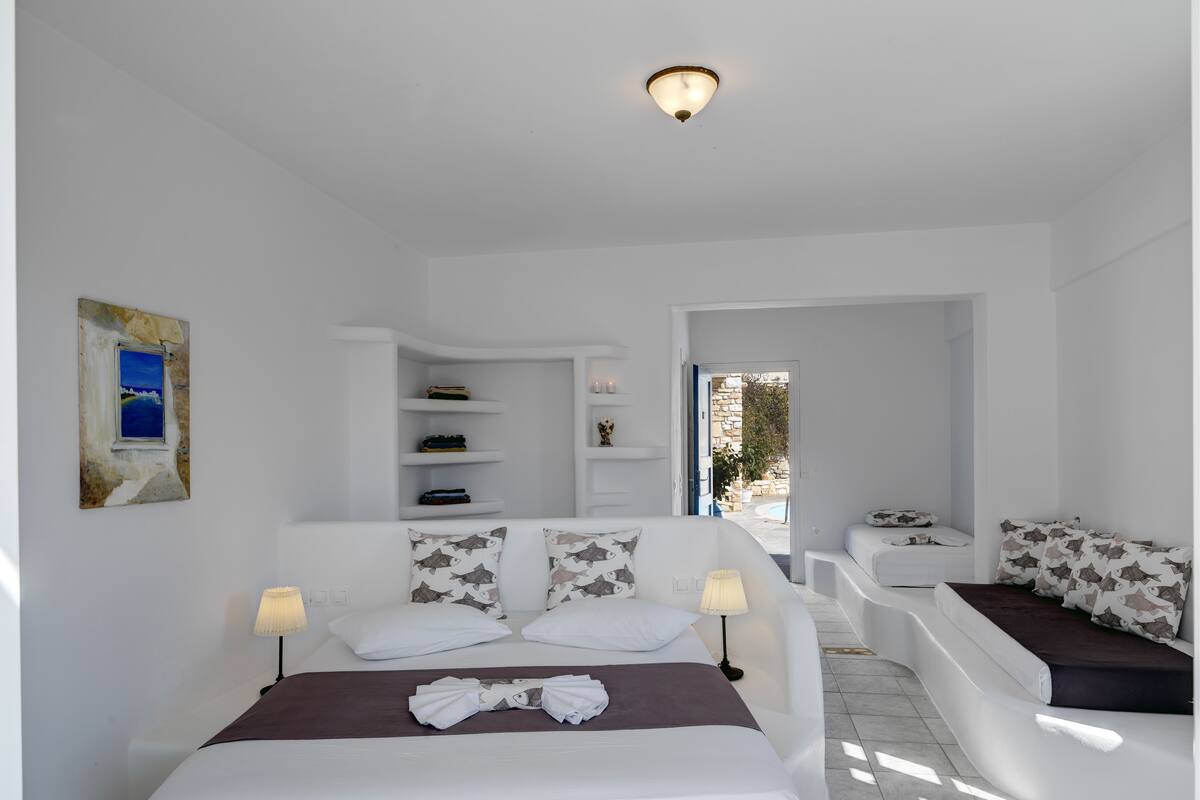 A modern, well-lit bedroom with a large bed, bedside tables, and a built-in shelf unit.