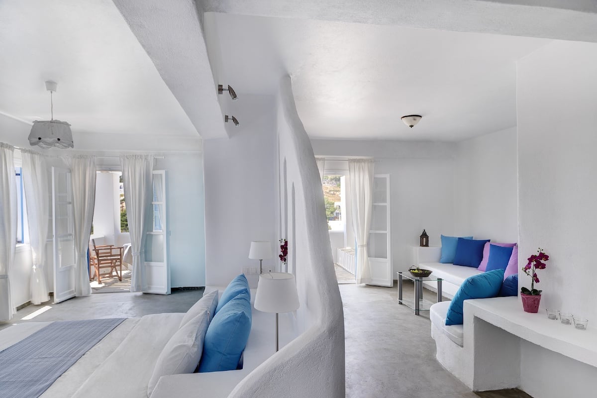 A modern, white-themed room with a bed, a sofa, and a dining area.