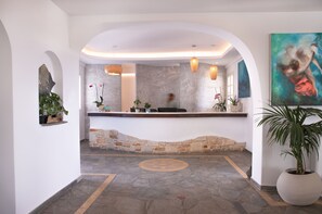 A reception area with a stone counter, potted plants, and a large painting on the wall. - Aloni Hotel (Paros)