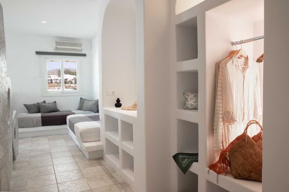 A modern bedroom with a bed, a seating area, and a wardrobe with clothes and a handbag.