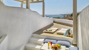 A balcony with a view of the sea, a table with fruits and drinks, and a sofa with cushions. - Aloni Hotel (Paros)