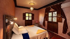 Un dormitorio con una cama, dos ventanas, una araña y una pequeña mesa con un florero.