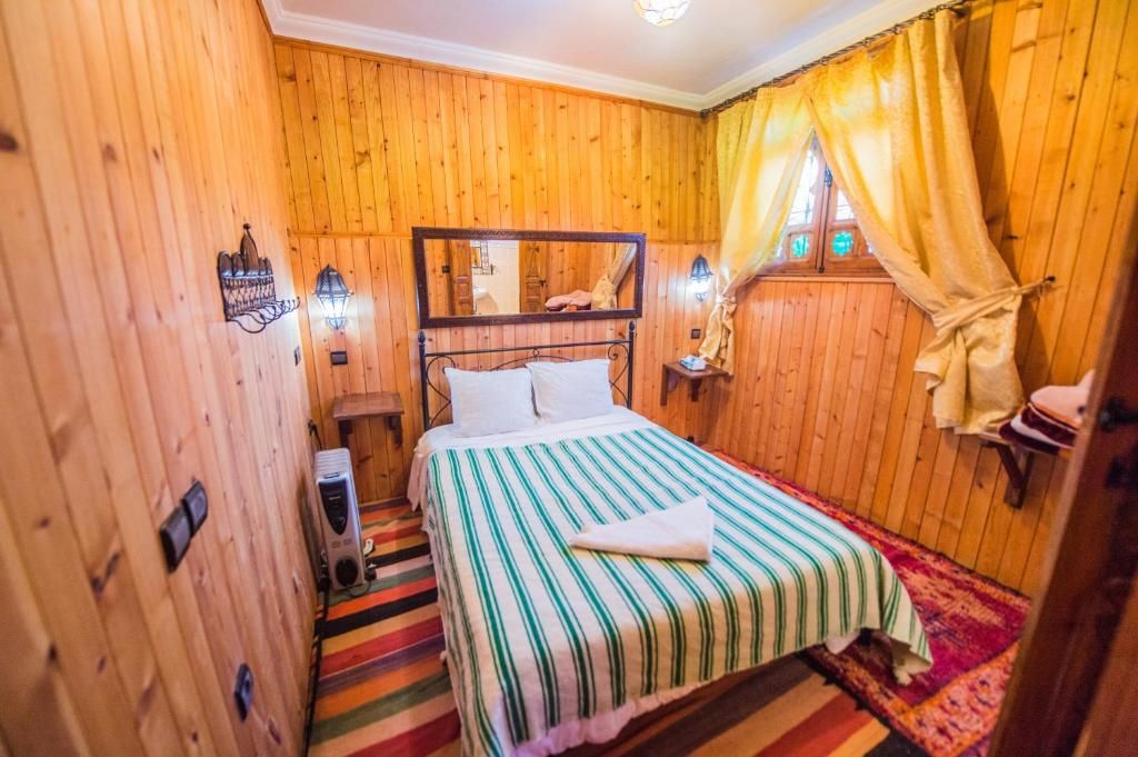 A wooden-paneled room with a bed, a nightstand, a lamp, and a window with curtains.