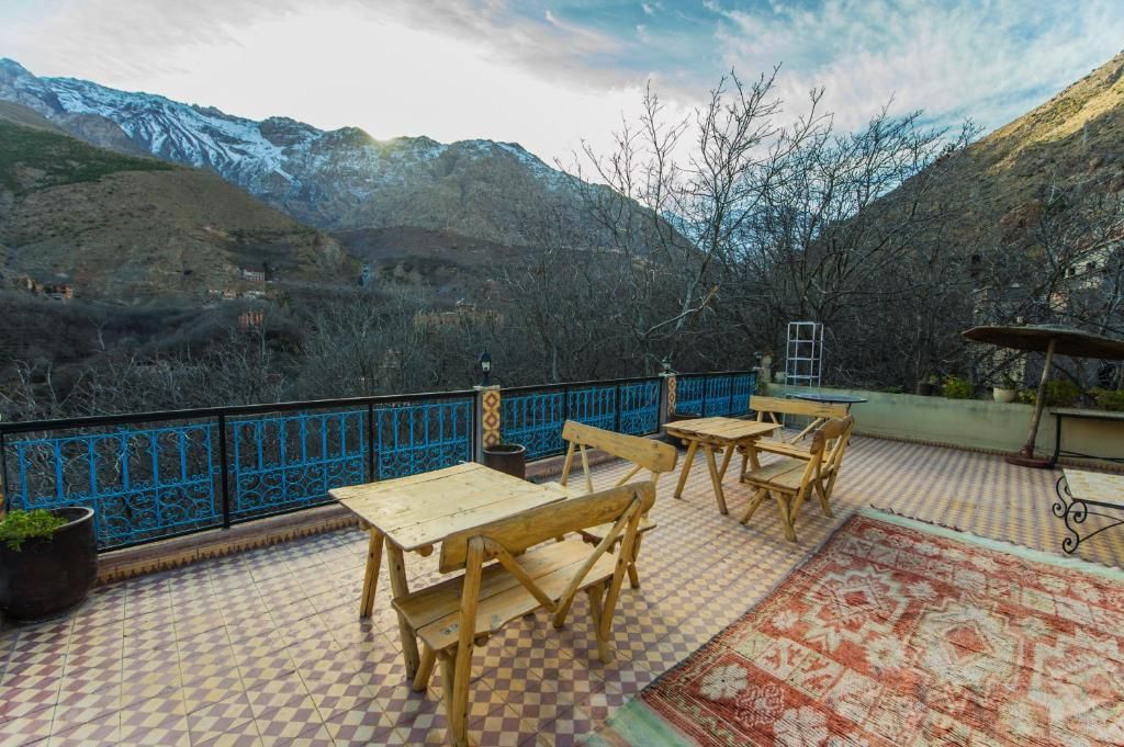 A terrace with wooden furniture and a patterned rug, overlooking a mountainous landscape.