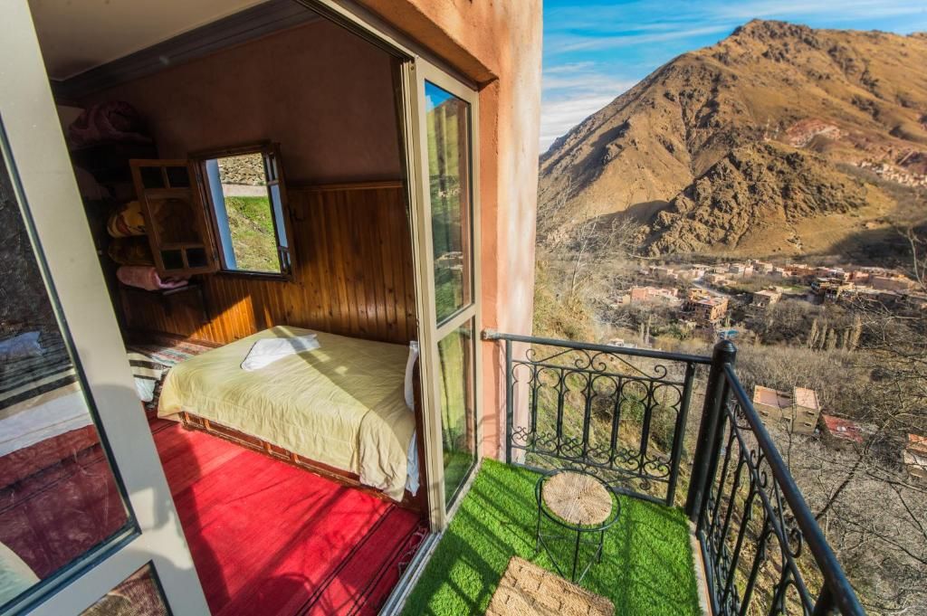 A balcony with a bed, a view of a mountainous landscape, and a village below.