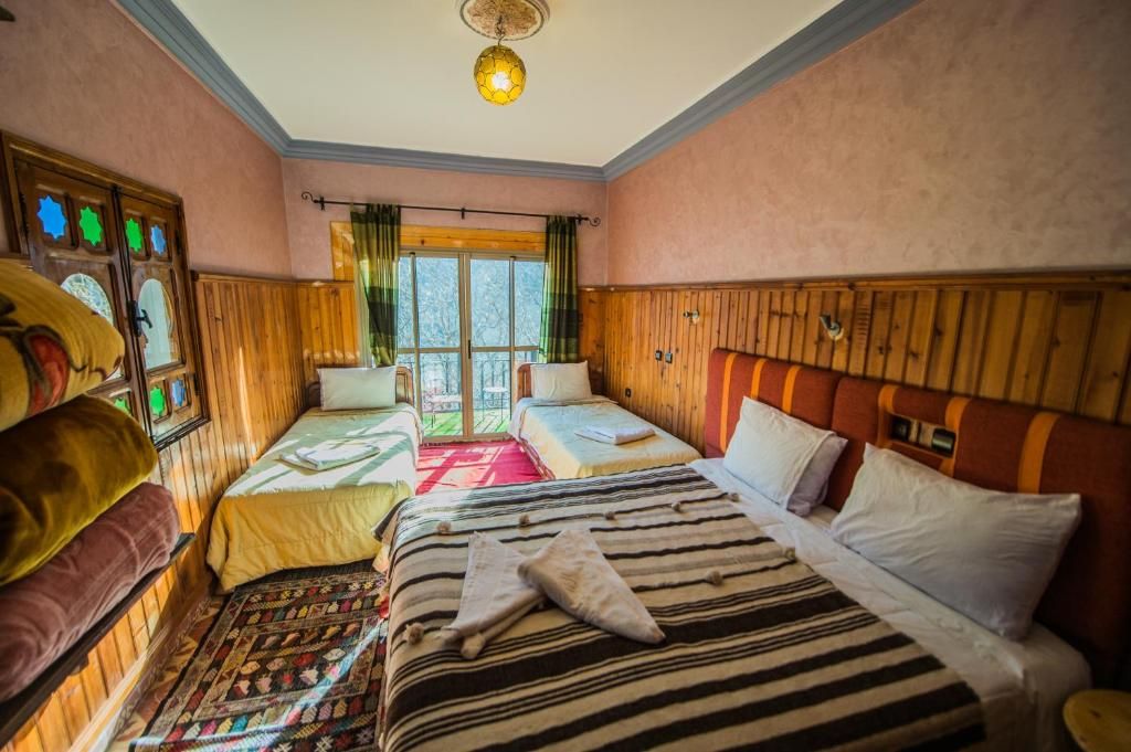 A hotel room with two single beds, a large bed, a wooden headboard, a window with curtains, and a patterned rug.