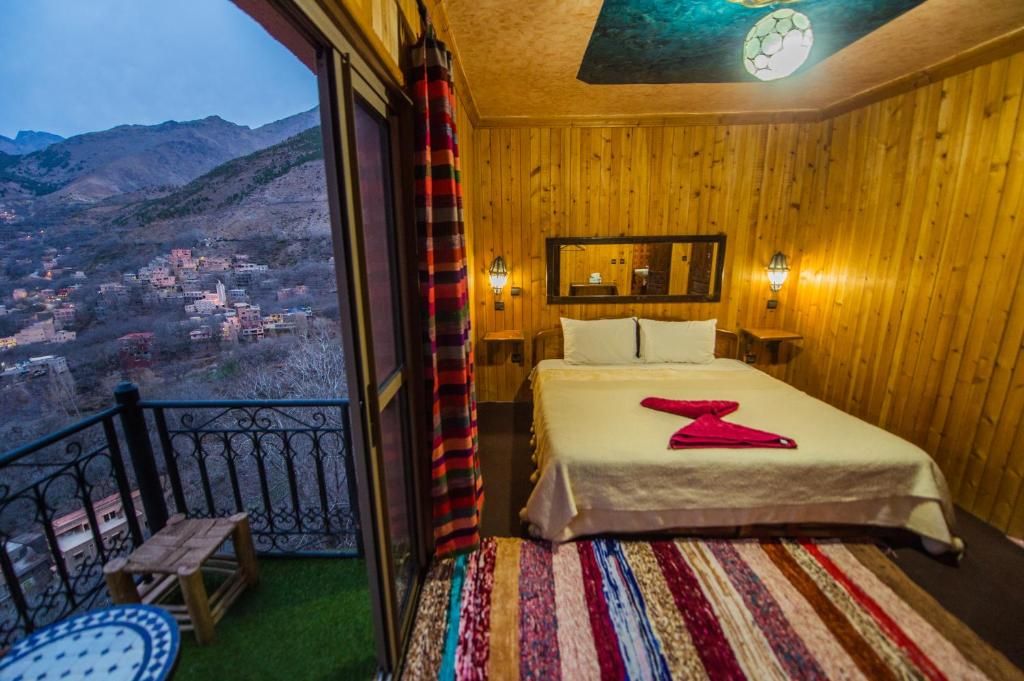 Ein Zimmer mit Bett, Blick auf ein Dorf und einem Balkon mit Geländer.