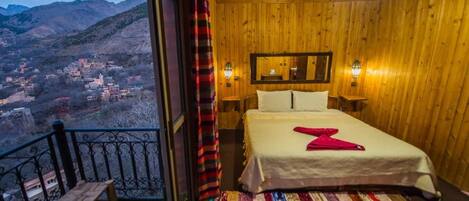 A room with a bed, a view of a village, and a balcony with a railing.