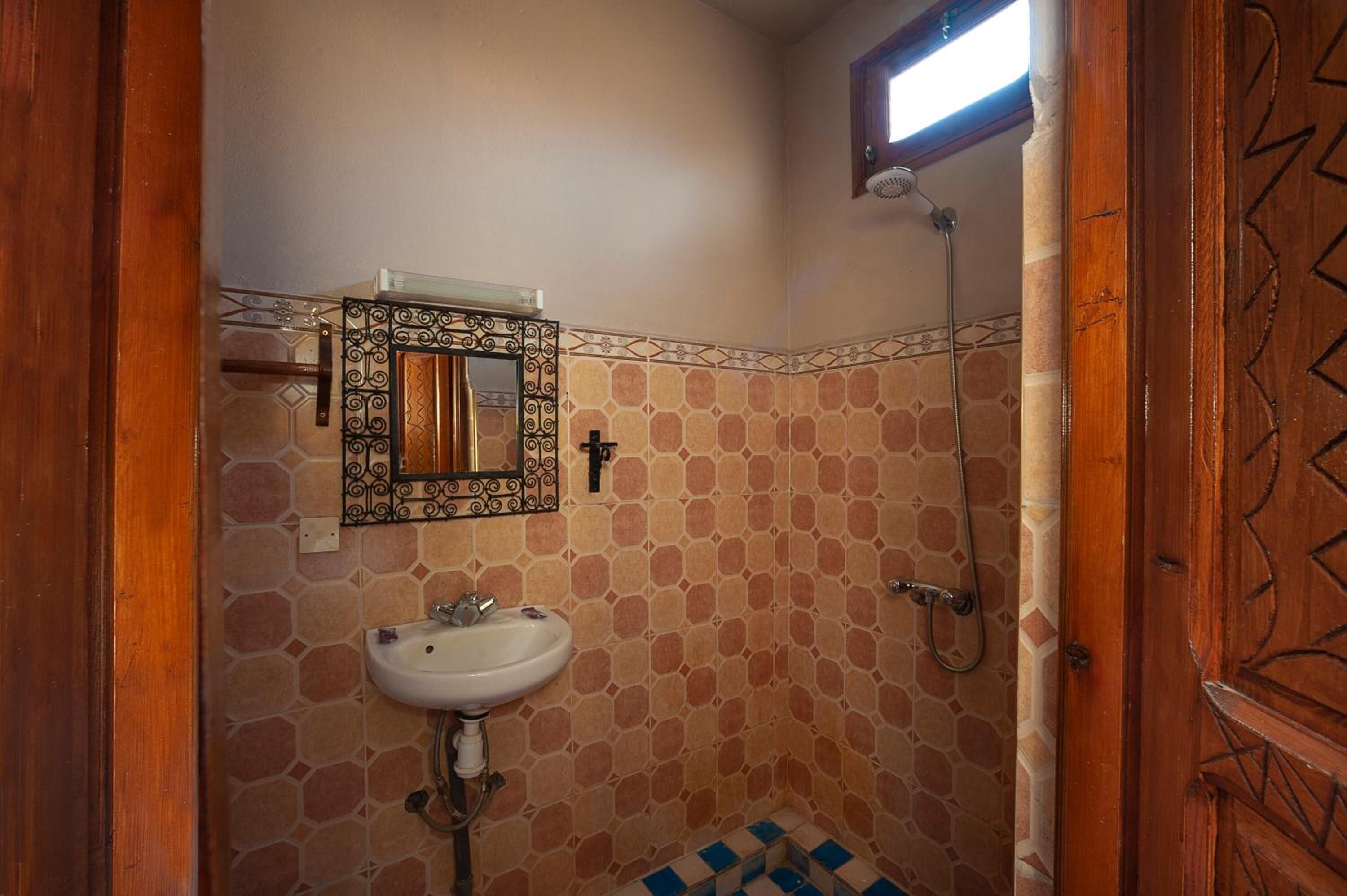 Un baño con piso de baldosas, un lavamanos, un espejo con marco decorativo y una ducha.
