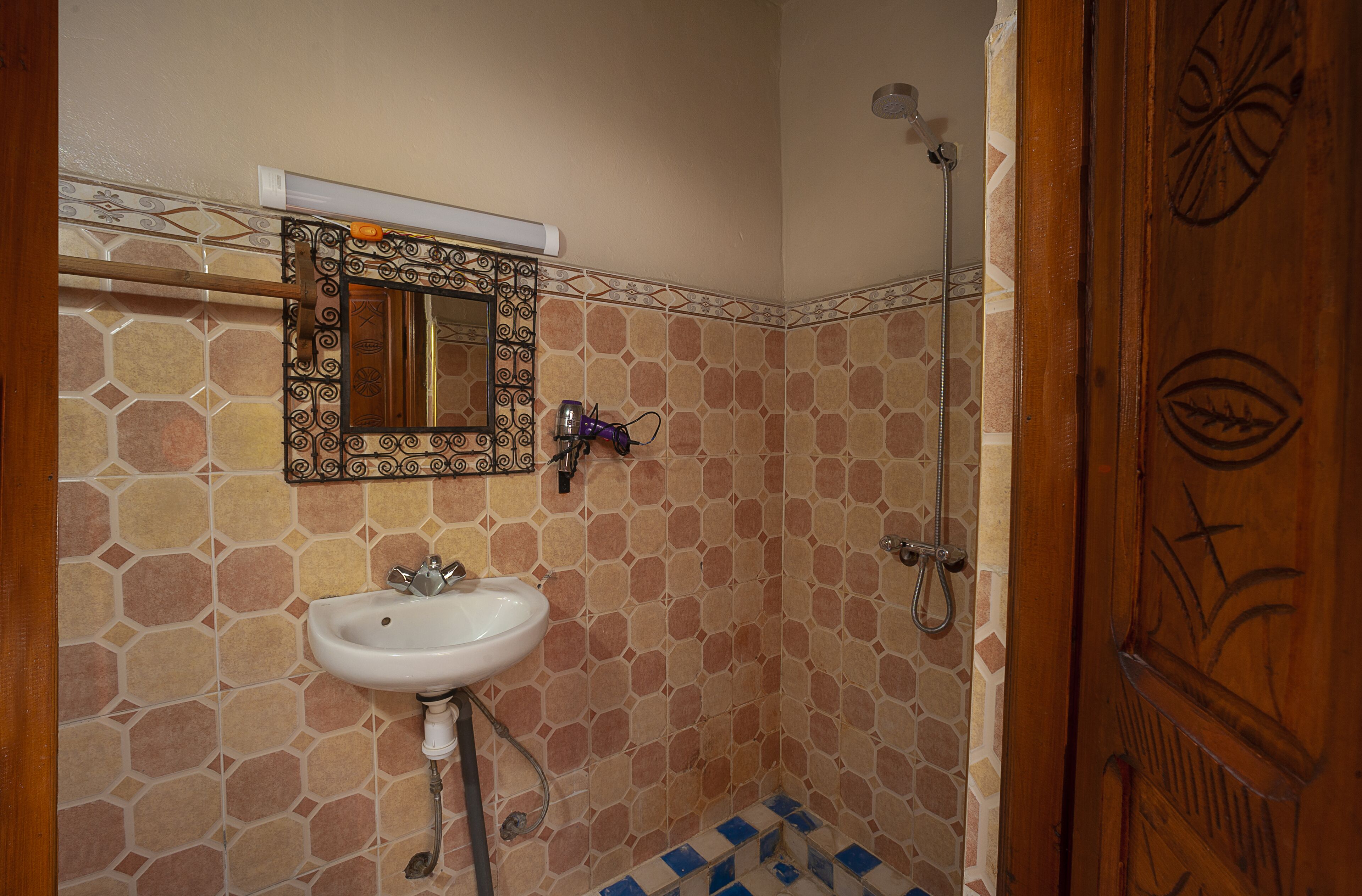 A bathroom with a tiled wall, a sink, a mirror, and a shower.