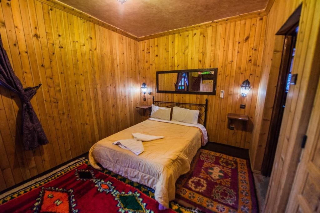 Una habitación con paneles de madera, una cama, dos lámparas de pared y un espejo.