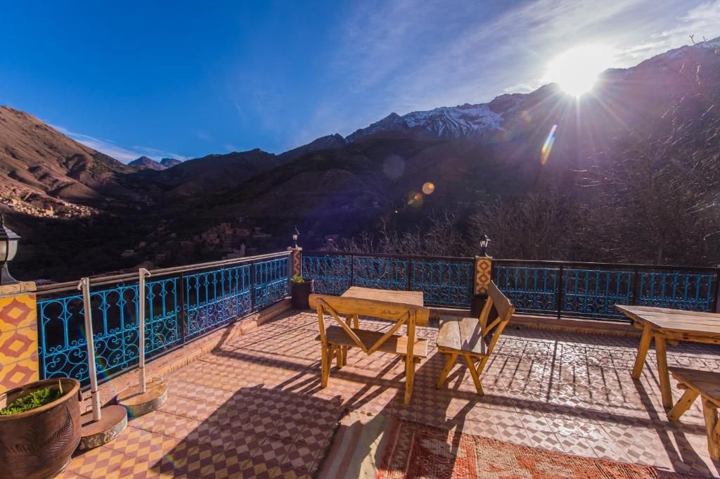 A terrace with a view of mountains, a blue railing, and wooden furniture.