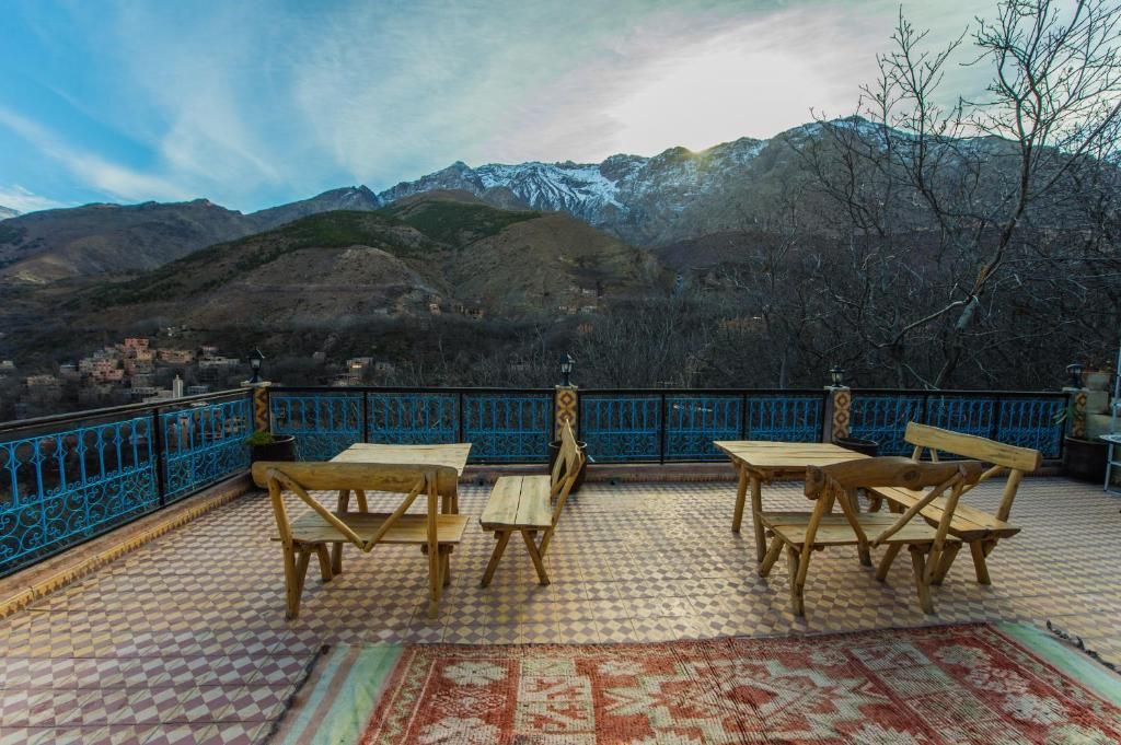 A terrace with wooden tables and chairs, a patterned floor, and a view of mountains in the background.
