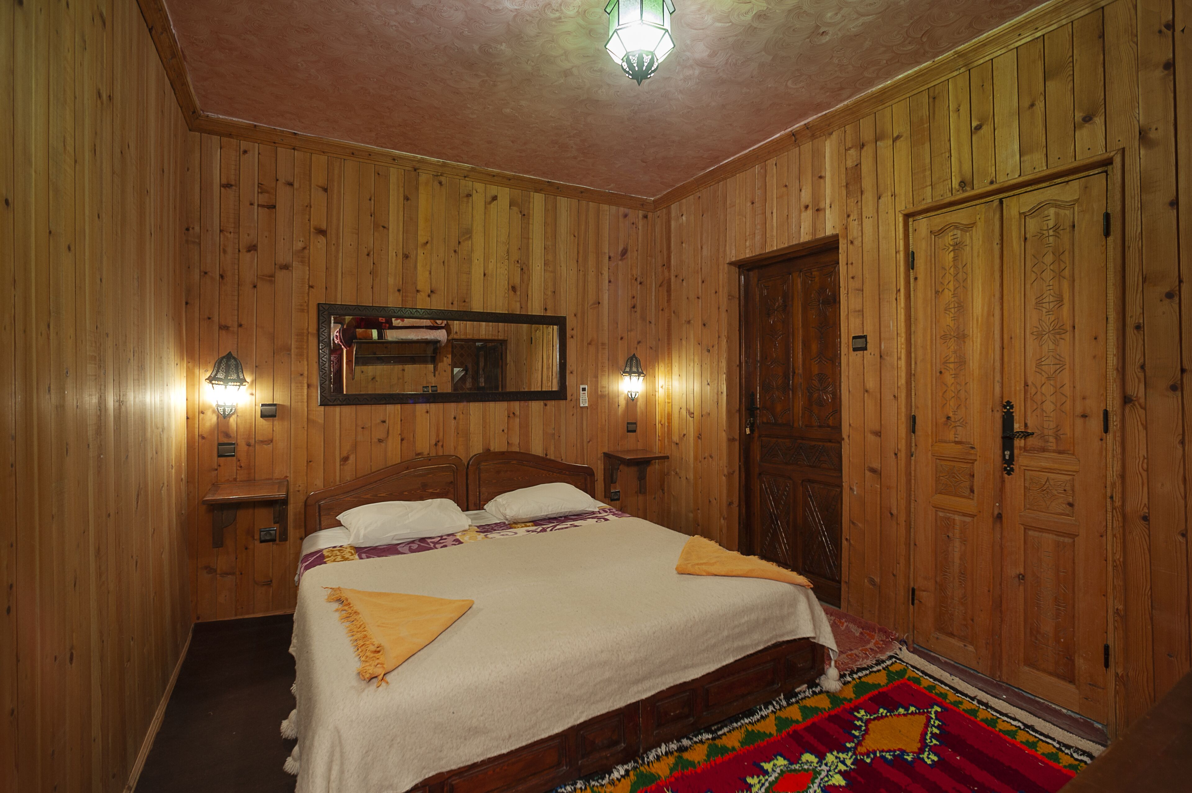 Un dormitorio con paneles de madera, una cama grande, dos mesitas de noche, un espejo y una puerta.