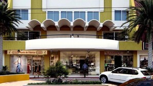 A hotel with a central entrance, two visible flags, and storefronts on either side. - Hotel Prado 72 (Barranquilla)