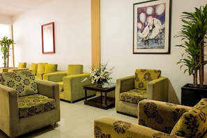 A hotel lobby with green upholstered sofas arranged around a central coffee table, a framed painting on the wall, and potted plants. - Hotel Prado 72 (Barranquilla)