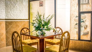A dining area with a wooden table and chairs, a floral centerpiece, and a view of the outside through a window. - Hotel Prado 72 (Barranquilla)