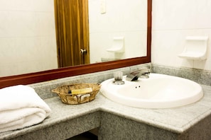 A bathroom with a white sink, a gold decorative basket, and a towel stack. - Hotel Prado 72 (Barranquilla)
