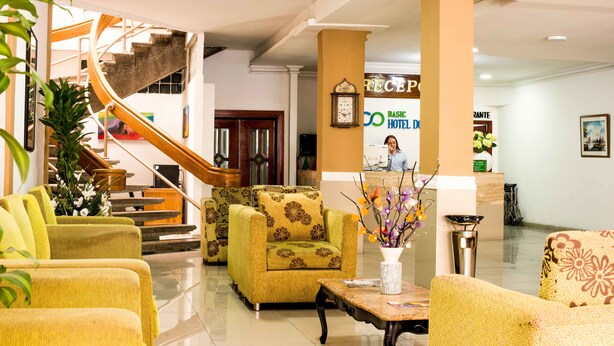 A hotel lobby with a staircase, seating area, reception desk, and a clock on the wall. - Hotel Prado 72 (Barranquilla)