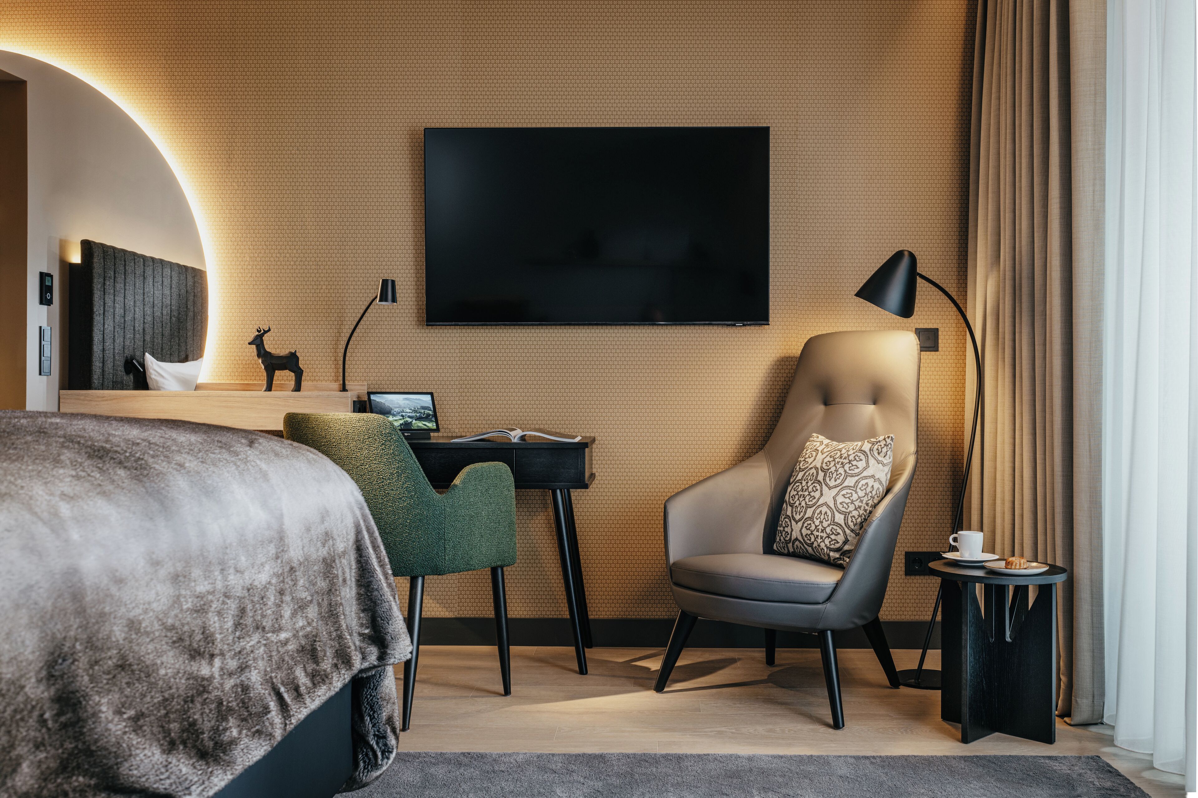 Una habitación de hotel moderna con una cama grande, un escritorio con una laptop, un sillón cómodo, un televisor y una lámpara.