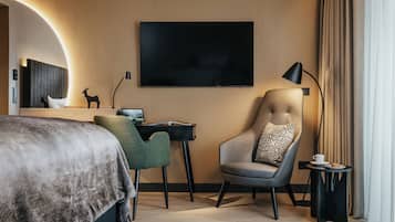 Una habitación de hotel moderna con una cama grande, un escritorio con una laptop, un sillón cómodo, un televisor y una lámpara.