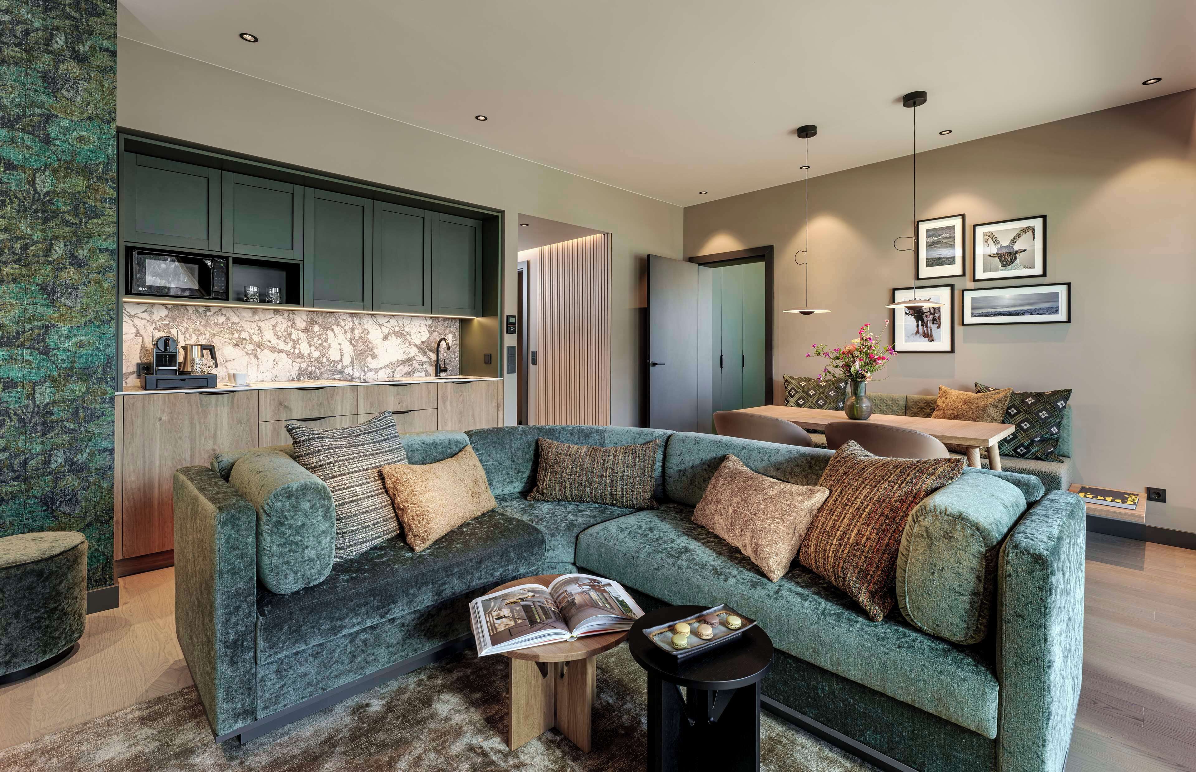 A modern living room with a sectional sofa, a coffee table, and a kitchen area with built-in appliances.
