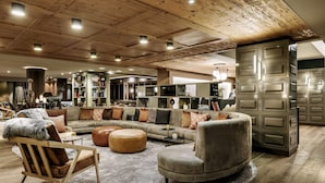 Un amplio salón con techo de madera, un sofá modular, un otoman redondos y un mueble empotrado.