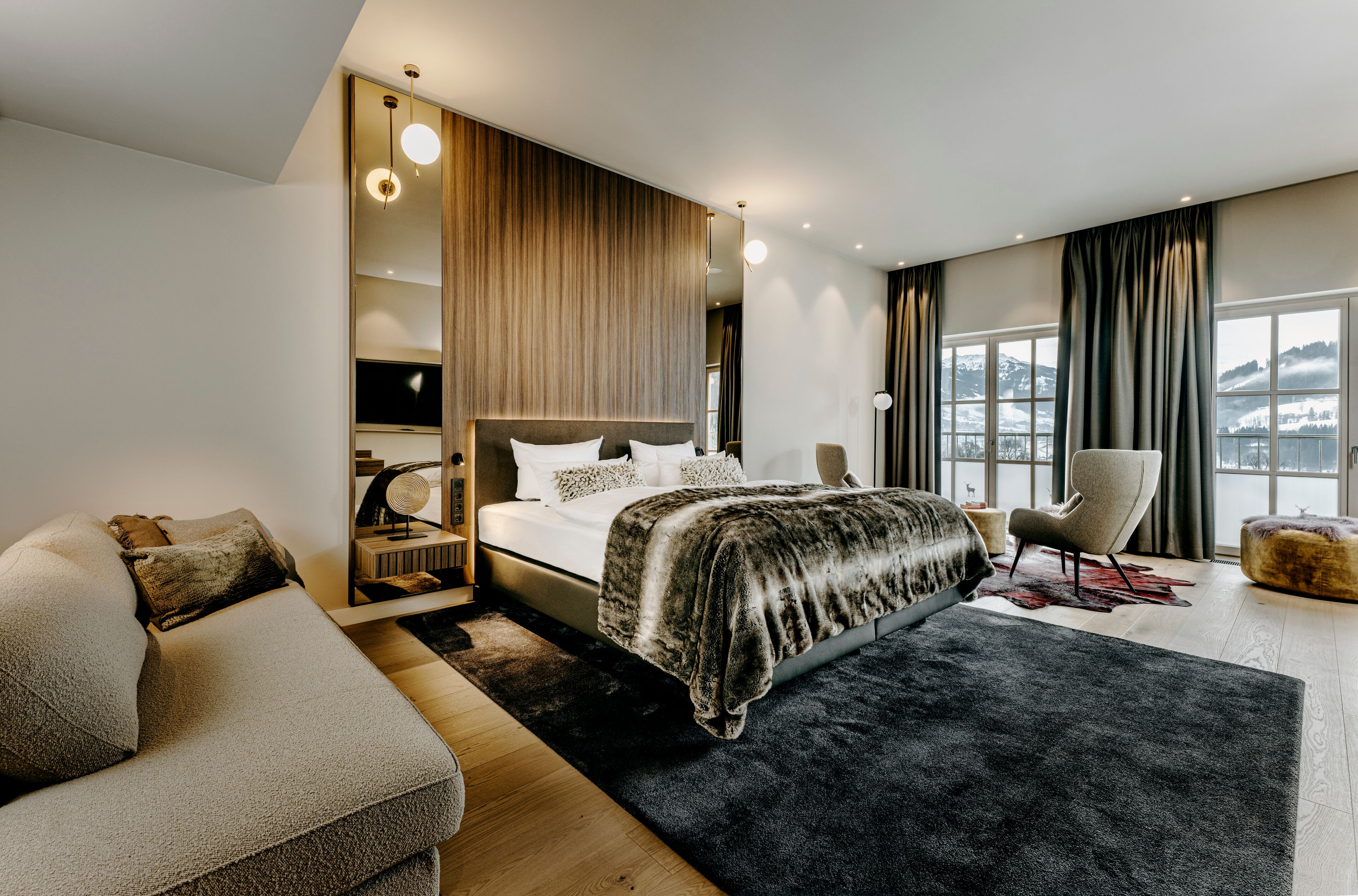 A modern bedroom with a large bed, a sofa, a chair, and a view of the outdoors.
