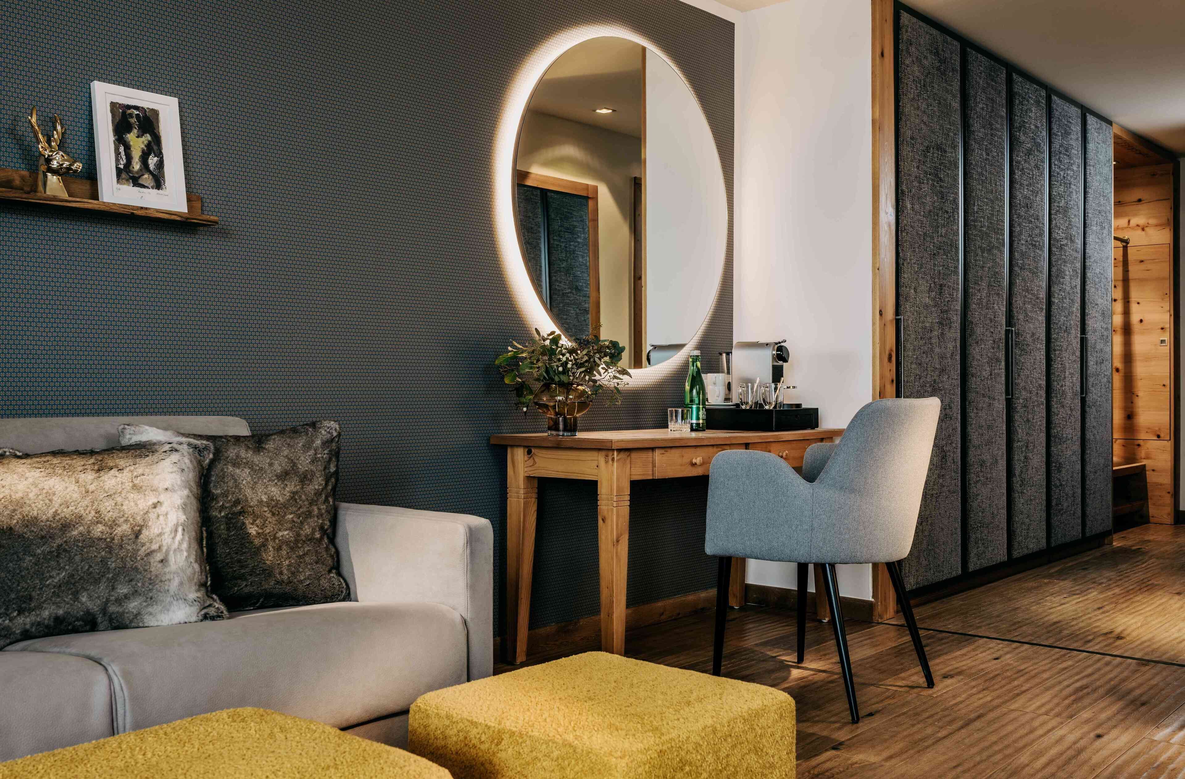 A modern room with a round mirror, a wooden desk, a grey chair, and a sofa with cushions.