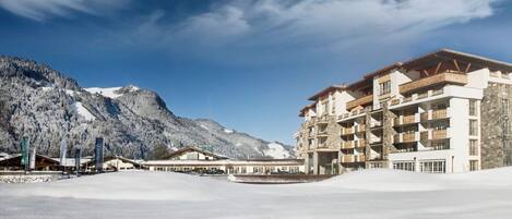 Een hotel met meerdere balkons, een bergachtige achtergrond en een besneeerd landschap.