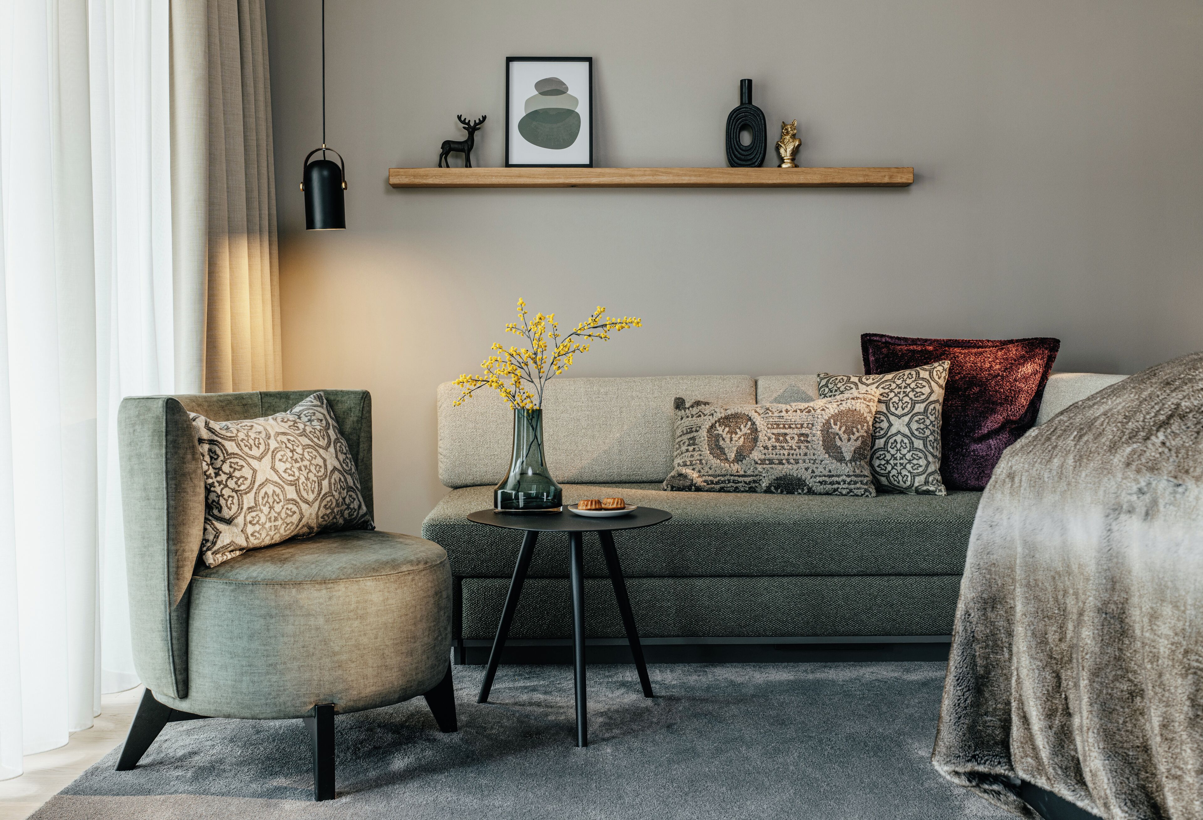 A modern living room with a sofa, armchair, and a small side table with a vase and a plate.